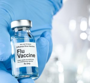 blue gloved hand holding a vial labelled 'Influenza Vaccine'