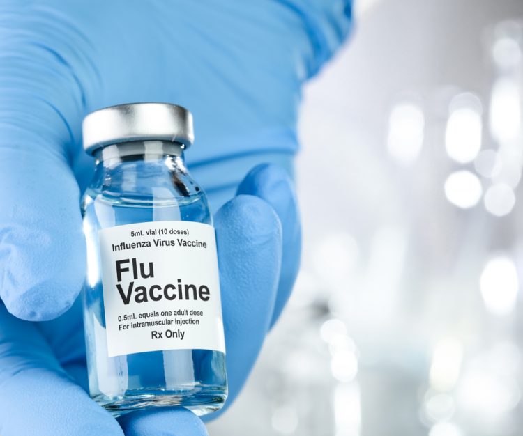 blue gloved hand holding a vial labelled 'Influenza Vaccine'