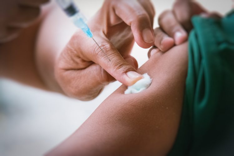 Doctor injecting a patient in the upper arm using a syringe