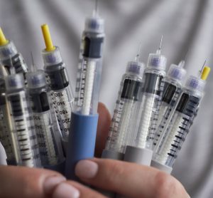 person in while coat holding syringes for self-injection of insulin