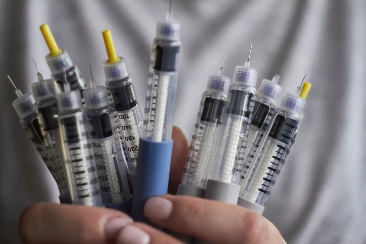 person in while coat holding syringes for self-injection of insulin