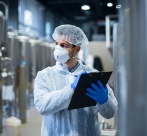 person wearing protective mask and white clothes holding checklist in factory - idea of facility inspections