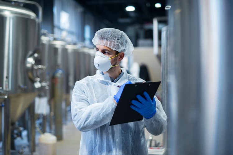 person wearing protective mask and white clothes holding checklist in factory - idea of facility inspections