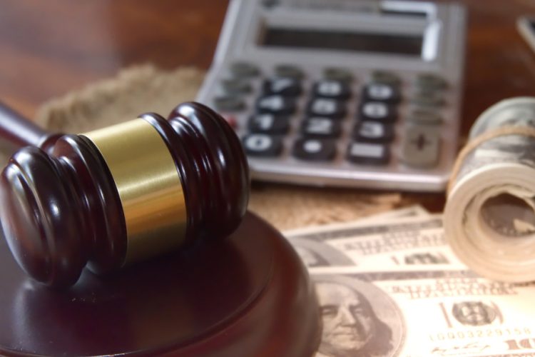 legal damages concept - wooden gavel and rolls of US bank notes with a calculator