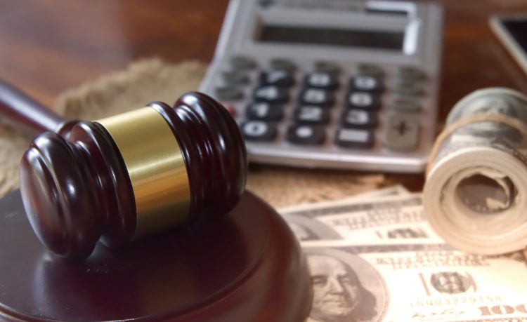 legal damages concept - wooden gavel and rolls of US bank notes with a calculator