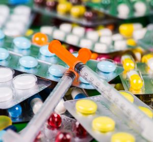 pile of various coloured tablets in blister packs with syringes on top