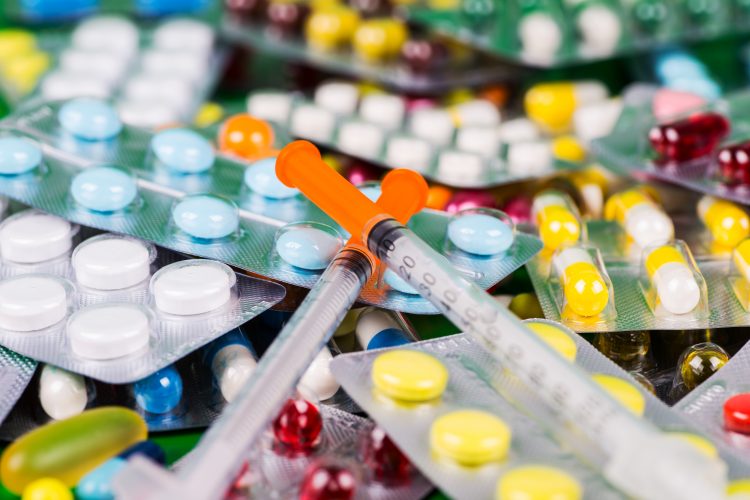 pile of various coloured tablets in blister packs with syringes on top