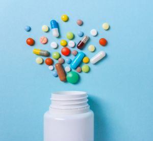 Assorted pharmaceutical pills, tablets and capsules spilling from a tipped over white bottle on a blue background