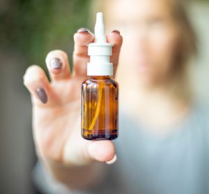 Female hand holding a nasal spray up close to the camera with background behind blurred