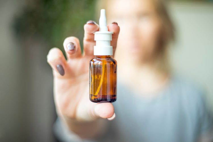 Female hand holding a nasal spray up close to the camera with background behind blurred