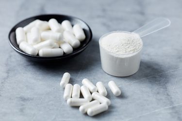 white capsules sat next to a measuring cup with white powder in - idea of active pharmaceutical ingredients