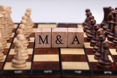 Wooden blocks spelling out M&A on a chess board - idea of strategic mergers and acquisitions