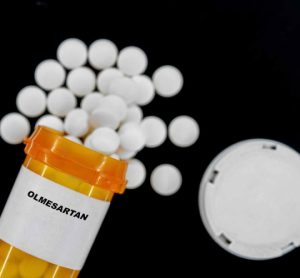 Olmesartan white pills spilling from an orange prescription medicines bottle