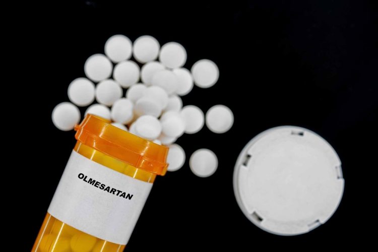 Olmesartan white pills spilling from an orange prescription medicines bottle