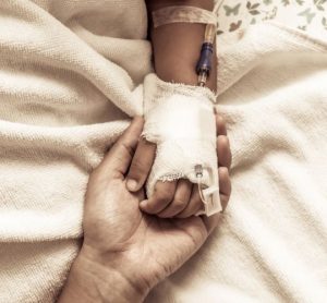 Close up of an adult holding the hand of a child recieving cancer treatment through IV - idea of paediatric oncology treatment