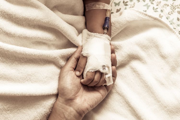 Close up of an adult holding the hand of a child recieving cancer treatment through IV - idea of paediatric oncology treatment