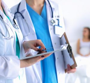 Young woman doctor holding a tablet and conferring with colleague with patient in bed blurred in background