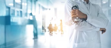 healthcare concept - male doctor in white coat with blurred hospital corridor as background