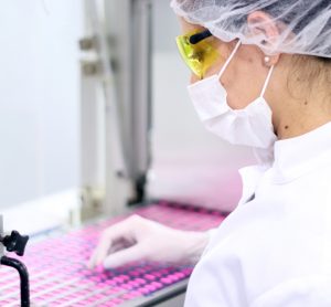 Worker pulling pink pills off of a production line for inspection/removal due to defects - idea of pharmaceutical QC