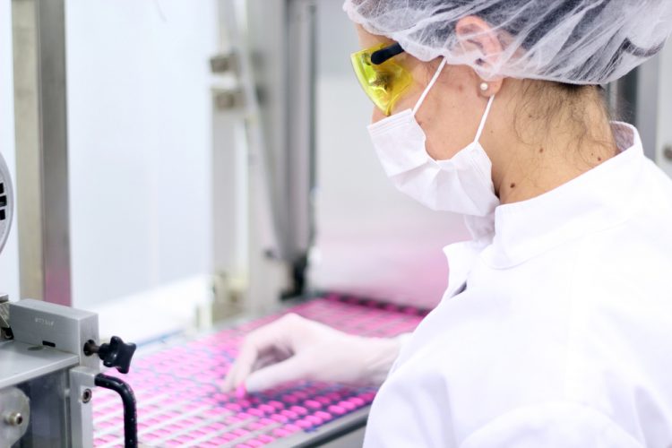 Worker pulling pink pills off of a production line for inspection/removal due to defects - idea of pharmaceutical QC