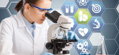 woman looking down a microscope with a graphic indicative of medical/pharmaceutical research behind