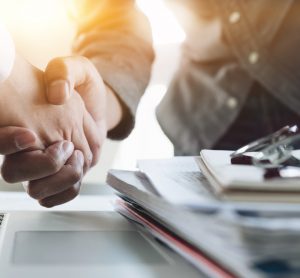 Close up of Business people shaking hands with a stack of paperwork and a stethoscope in frame - idea of pharmaceutical/medical mergers and acquisitions