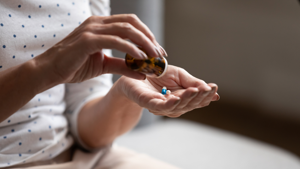 woman pouring blue and white capsules from a brown glass bottle to take medication