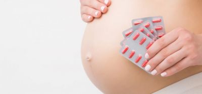 concept of including pregnant women in clinical research - close up of pregnant woman's stomach with blister packs of red pills held up next to it