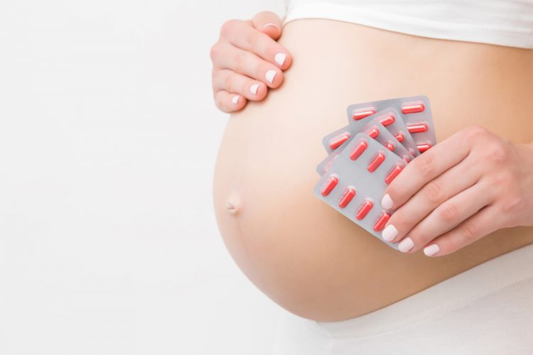 concept of including pregnant women in clinical research - close up of pregnant woman's stomach with blister packs of red pills held up next to it