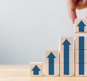 Hand stacking wooden blocks with arrows on them to create a series of upward steps - idea of revenue growth/financial results