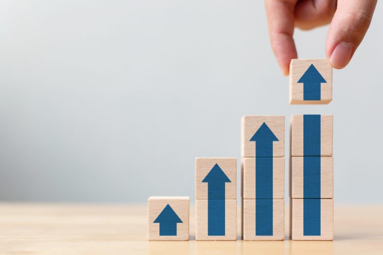 Hand stacking wooden blocks with arrows on them to create a series of upward steps - idea of revenue growth/financial results