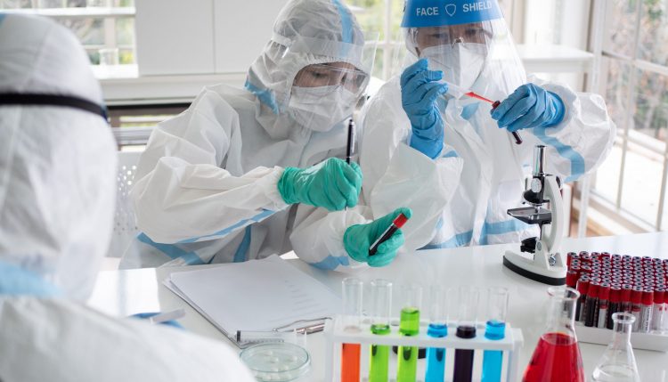 scientists in full PPE looking at COVID-19 blood samples - could be testing vaccine immunogenicity