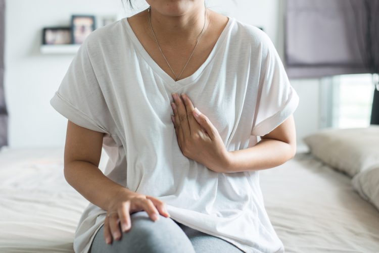 Woman in pain touching chest where oesophagus is