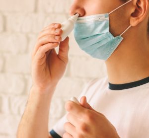 Man with face mask using nasal spary