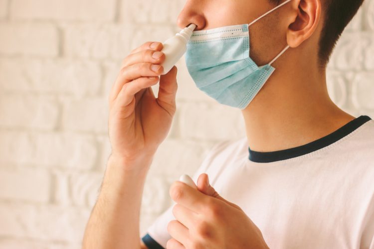 Man with face mask using nasal spary