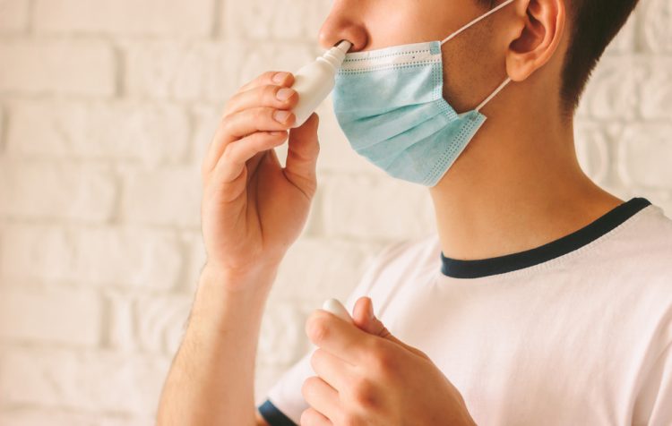 Man with face mask using nasal spary