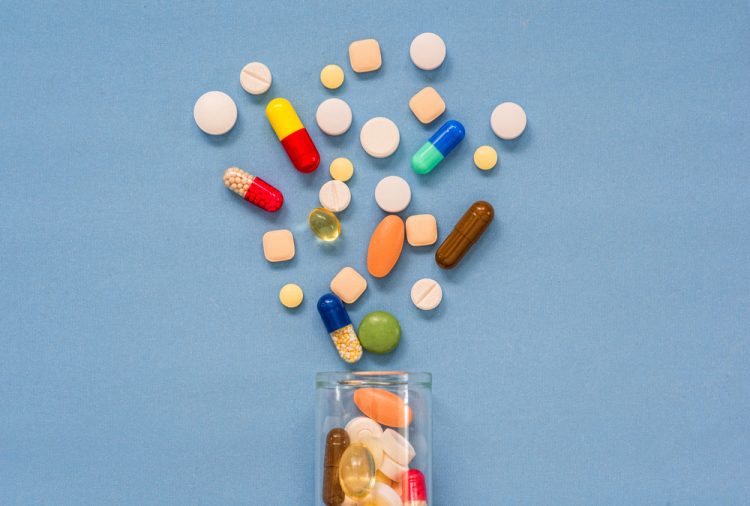 Drug pills spilling out of bottle on blue background