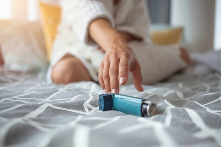 Woman reaching for asthma pump on bed