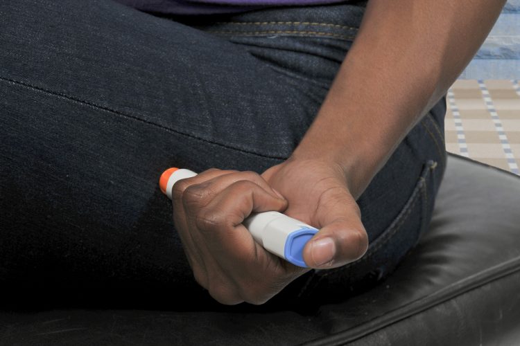 woman using an adrenaline autoinjector (a kind of smart syringe) on her thigh