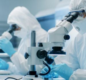 two scientists wearing sterile clothing performing research using microscopes in a cleanroom environment - idea of sterilisation