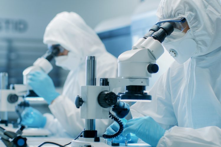 two scientists wearing sterile clothing performing research using microscopes in a cleanroom environment - idea of sterilisation