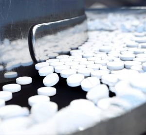 White tablets flowing along a stainless steel production line - idea of tableting/pharmaceutical production