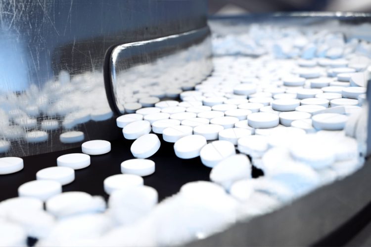 White tablets flowing along a stainless steel production line - idea of tableting/pharmaceutical production