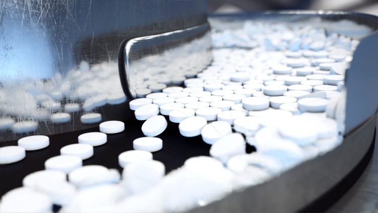 White tablets flowing along a stainless steel production line - idea of tableting/pharmaceutical production