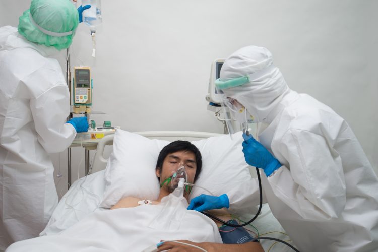 man with COVID-19 in a hospital bed, with an oxygen mask on with doctors checking his IV