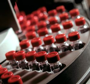 close up of red topped glass vials filled with liquid on a production line- vaccine manufacturing