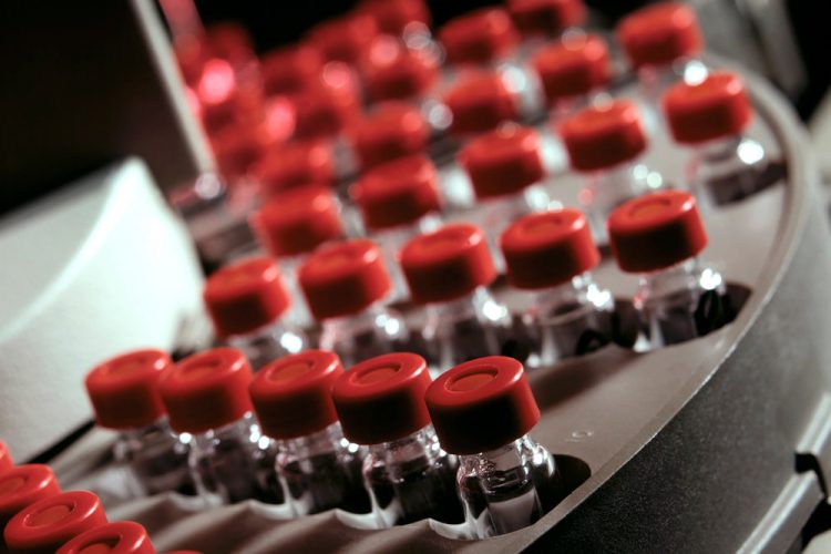close up of red topped glass vials filled with liquid on a production line- vaccine manufacturing