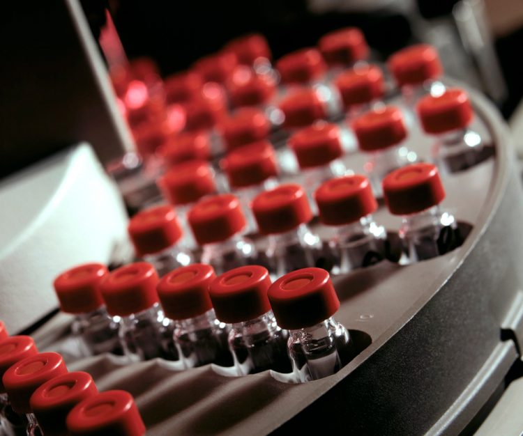 close up of red topped glass vials filled with liquid on a production line- vaccine manufacturing