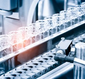 Idea of vaccine manufacturing - Glass bottles in production in the tray of an automatic liquid dispenser; a line for filling medicines such as vaccines