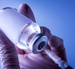 close up of a syringe drawing a vaccine dose from a glass vial